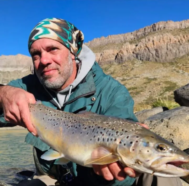 Pescador con pañuelo en la cabeza mostrando una trucha marrón