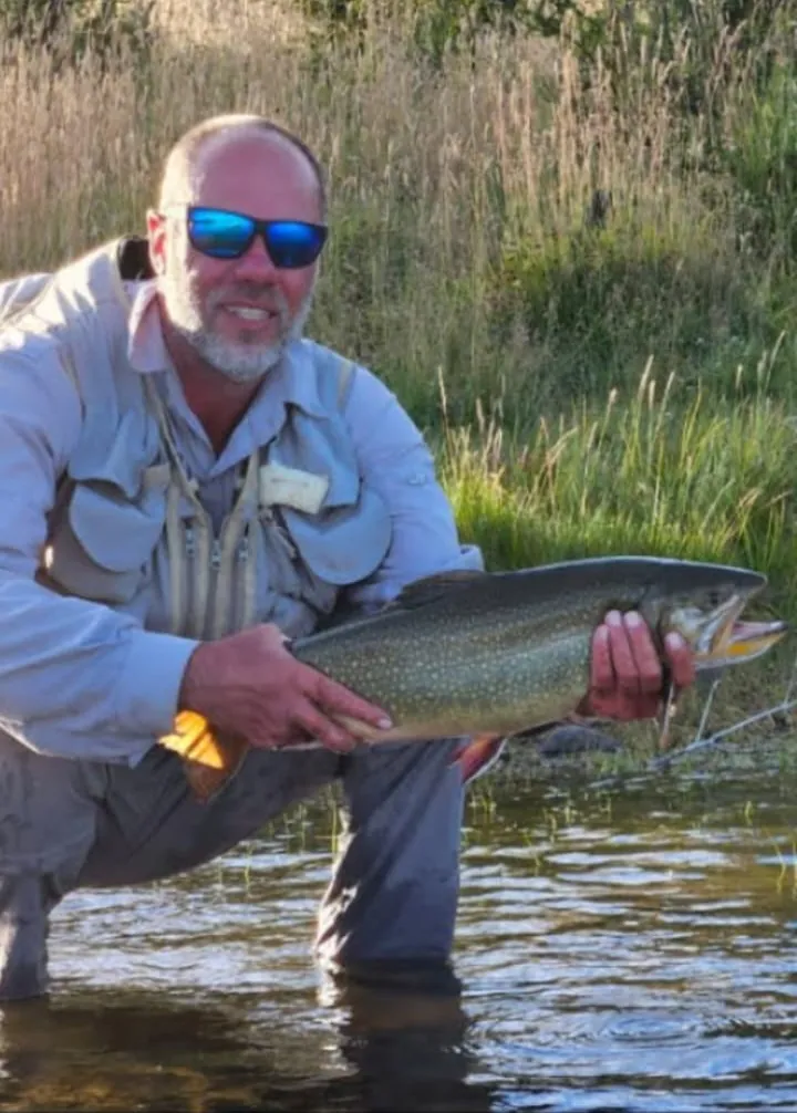 Pescador arrodillado en el río sosteniendo una trucha grande